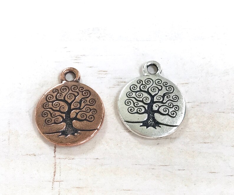Puede incluir: Dos abalorios plateados con un dise&ntilde;o de &aacute;rbol de la vida. Un abalorio es de color cobre y el otro es plateado.