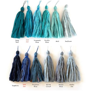 May include: Twelve fabric tassels arranged in two rows, featuring shades of blue, teal, and gray. Labels include Deep Teal, Sold Out, Yosemeti Blue, Pacific Blue, Mint, Seafoam, Sapphire, Sold Out, Prussian Blue, Storm Cloud, Ocean Blue, and Arctic Ice.