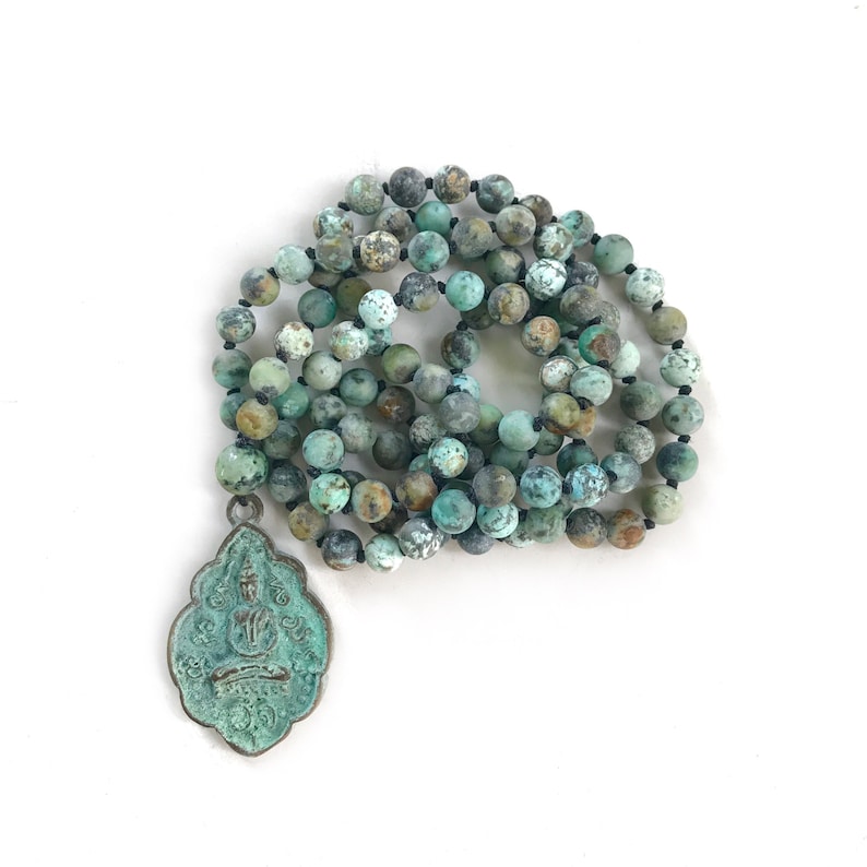 May include: A turquoise and brown beaded necklace with a metal pendant. The pendant is shaped like a teardrop and has intricate designs on it.
