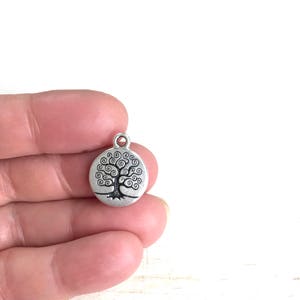 Puede incluir: Encanto de plata con un dise&ntilde;o de &aacute;rbol de la vida. El &aacute;rbol est&aacute; estilizado con ramas en espiral y un tronco grueso. El encanto es redondo y tiene un bucle en la parte superior para sujetarlo a un collar o pulsera.