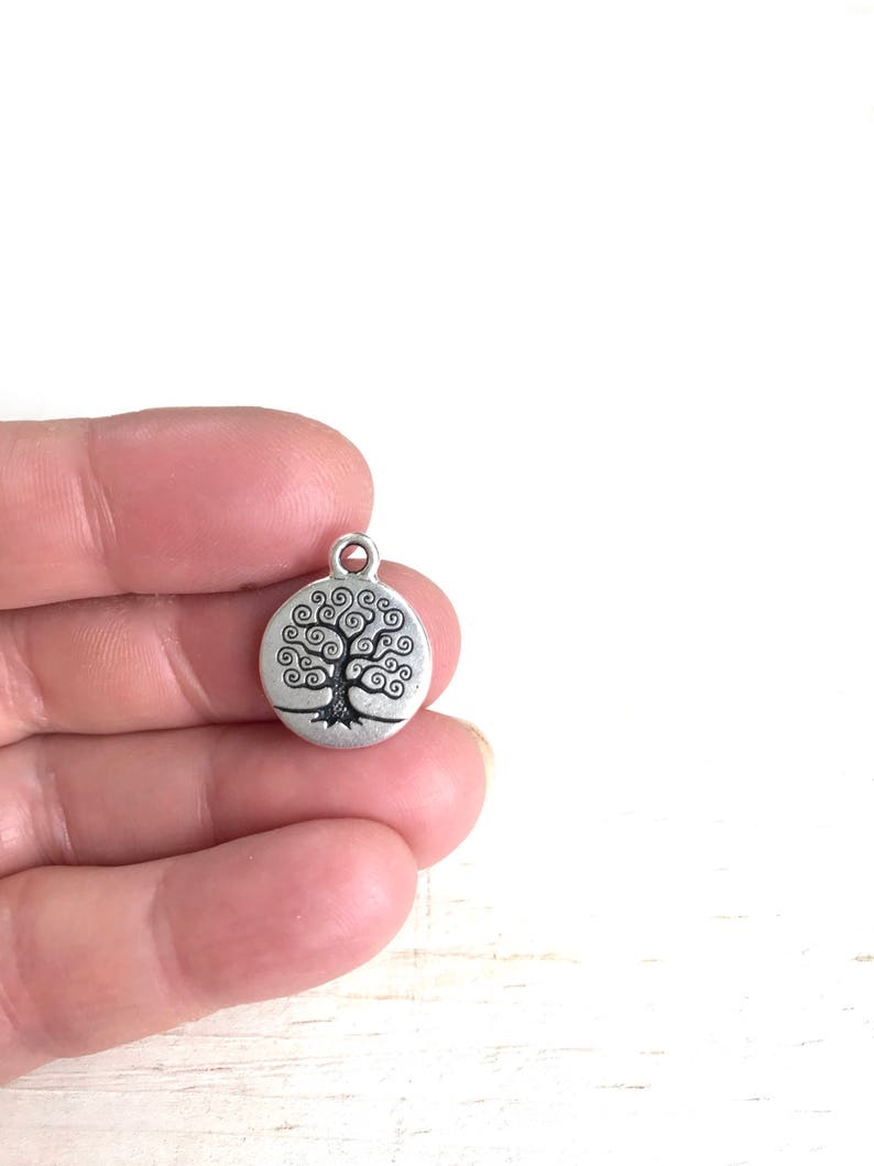 Puede incluir: Encanto de plata con un dise&ntilde;o de &aacute;rbol de la vida. El &aacute;rbol est&aacute; estilizado con ramas en espiral y un tronco grueso. El encanto es redondo y tiene un bucle en la parte superior para sujetarlo a un collar o pulsera.