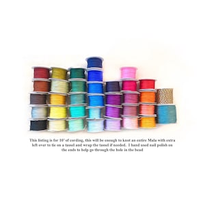 May include: A collection of thirty-two spools of colorful cording arranged in rows. The text below reads: This listing is for 10' of cording, this will be enough to knot an entire Mala with extra left over to tie on a tassel and wrap the tassel if needed. I hand used nail polish on the ends to help go through the hole in the bead.