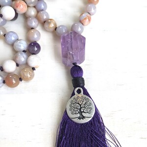 Puede incluir: Un collar mala de piedras preciosas de &aacute;gata p&uacute;rpura y marr&oacute;n con un colgante de amatista y un dije de &aacute;rbol de la vida plateado. El collar tiene una borla morada.