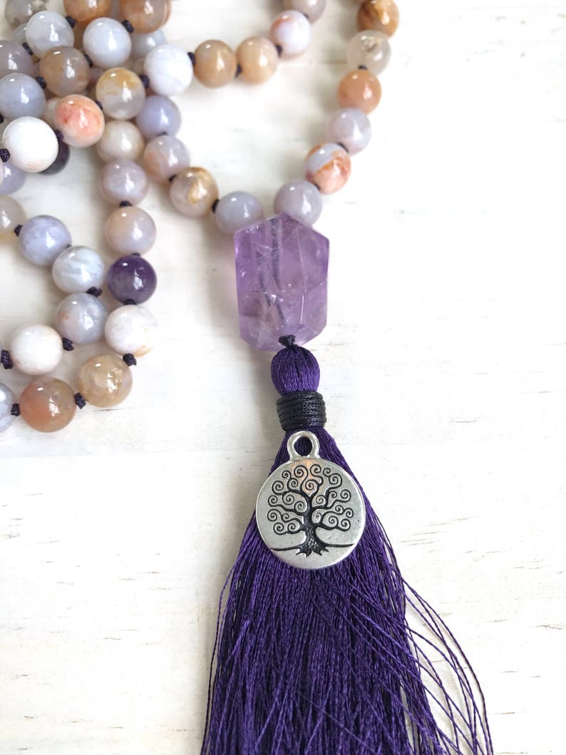 Puede incluir: Un collar mala de piedras preciosas de &aacute;gata p&uacute;rpura y marr&oacute;n con un colgante de amatista y un dije de &aacute;rbol de la vida plateado. El collar tiene una borla morada.