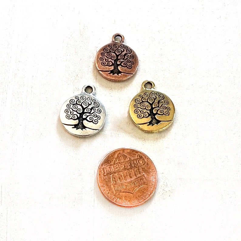 Puede incluir: Tres abalorios redondos de metal con un dise&ntilde;o de &aacute;rbol de la vida. Los abalorios son de plata, oro y cobre.