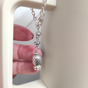 May include: Silver pineapple charm necklace with a silver chain and two silver beads.