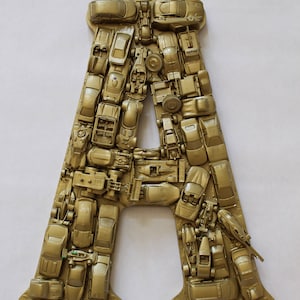 May include: A gold letter A made from toy cars. The letter is made of a variety of different car models, all painted gold.