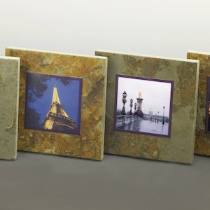 May include: Four square slate coasters with a rustic brown and gold finish. Each coaster features a different black and white photograph of a famous Parisian landmark, including the Eiffel Tower, Notre Dame Cathedral, and the Seine River.