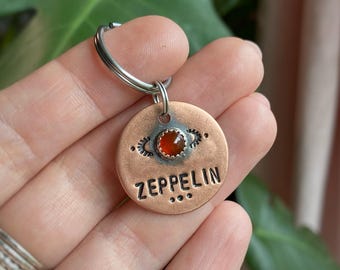 May include: Copper dog tag with a red gemstone and the word "ZEPPELIN" engraved on it.