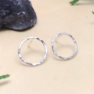 May include: A pair of silver hammered circle stud earrings. The earrings are simple and minimalist, making them a versatile accessory for any occasion.