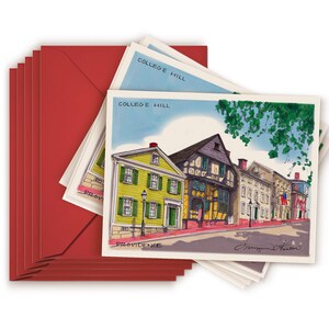 May include: A stack of red envelopes with white postcards inside. The postcards feature a watercolor illustration of a row of colorful historic buildings in Providence, Rhode Island. The text on the postcards reads "College Hill, Providence".