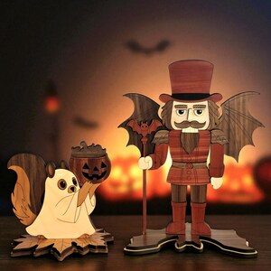 May include: Wooden Halloween decorations featuring a squirrel in a ghost costume holding a pumpkin bucket and a nutcracker with bat wings and a top hat. The decorations are made of wood and have a warm color palette.