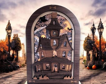 May include: A wooden, layered haunted house decoration. The brown house has multiple stories, windows, and a porch. It is set inside a wooden arch with a night sky scene. The base is dark, and the background shows a cobblestone path and street lamps.