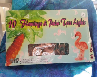 May include: A box of Golden Light brand string lights featuring 10 flamingo and palm tree-shaped lights. The box has a light blue background with pink flamingo silhouettes. The text on the box reads "10 Flamingo & Palm Tree Lights."