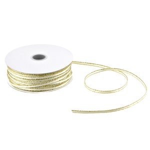 May include: A spool of white satin ribbon with a gold metallic edge. The ribbon is wound around a white cardboard spool.
