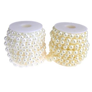 May include: Two spools of white pearl trim, each wrapped in white plastic. The pearl trim is made of small, round, white pearls.