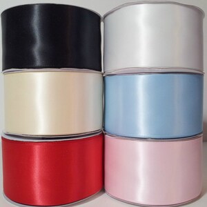 May include: Six spools of satin ribbon in various colors. The spools are arranged in a row, with the black spool on the left and the pink spool on the right. The colors are black, ivory, light blue, red, and pink.
