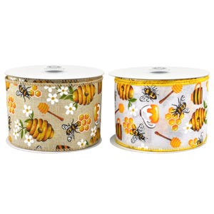 May include: Two spools of decorative ribbon with a bee theme. One spool has a tan background with bees, honeycombs, flowers, and honey dippers. The other spool has a white background with yellow trim and the same bee-themed design.