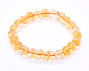 May include: A circular bracelet composed of translucent, spherical yellow beads. Each bead features internal golden-orange inclusions and natural variations in clarity. The beads are strung together on a thin, visible orange elastic cord.
