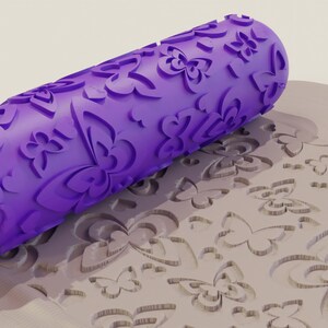 May include: Purple rolling pin with a butterfly design. The rolling pin is rolling over a surface that has been embossed with the same butterfly design.