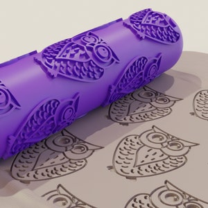 May include: Purple rolling pin with an owl design. The rolling pin is rolling over a surface with a repeating pattern of owls.