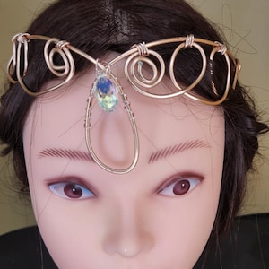 May include: A gold wire headband with a teardrop-shaped crystal in the center. The headband is made of wire that is twisted into a spiral design.