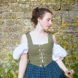 May include: A woman wearing a green, off-the-shoulder,  linen bodice with white puffed sleeves and a plaid skirt.