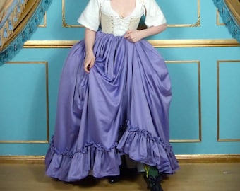 May include: A woman wearing a white corset and a long, flowing purple skirt with ruffles. The skirt is gathered at the waist and has a large, flowing train. The woman is standing in front of a blue and gold wall.