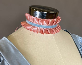 May include: A light blue satin dress with a ruffled pink and blue ribbon choker. The dress has a lace-up bodice with gold and white embellishments.