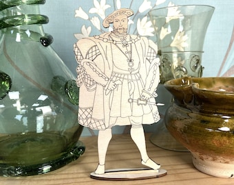 Puede incluir: Un recorte de madera de un hombre con una túnica estampada y una corona. El recorte está de pie sobre una base de madera. El fondo incluye una botella de vidrio verde, una copa de vidrio transparente y un cuenco de cerámica marrón.