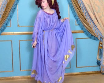 May include: A woman wearing a purple gown with gold accents. The gown is flowing and has a loose fit. The woman has red hair and is wearing a gold headband.