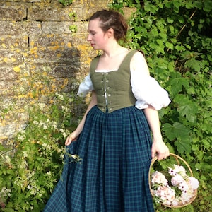 May include: A woman wearing a green and white dress with a plaid skirt and a basket of flowers in her hand.