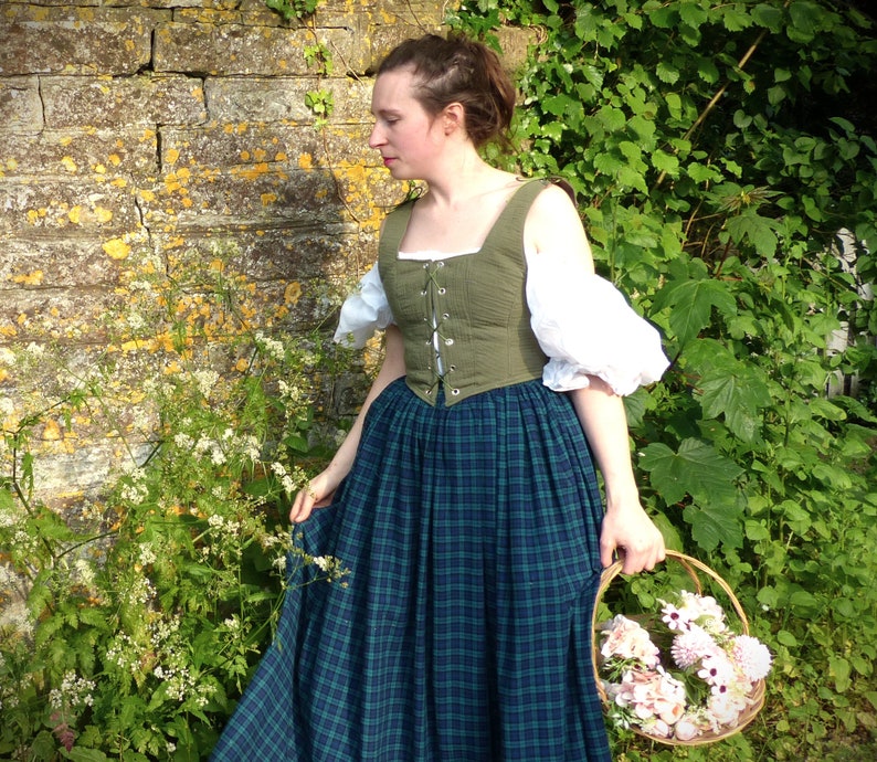 May include: A woman wearing a green and white dress with a plaid skirt and a basket of flowers in her hand.