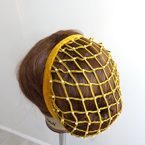 以下が含まれることがあります： ベルベットのバンドと白い真珠のアクセントが付いた黄色のヘアネット。ネットは細かいメッシュ素材で作られており、髪を固定するように設計されています。