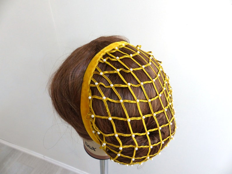 以下が含まれることがあります： ベルベットのバンドと白い真珠のアクセントが付いた黄色のヘアネット。ネットは細かいメッシュ素材で作られており、髪を固定するように設計されています。