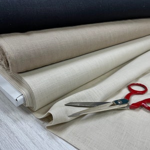 May include: A stack of fabric rolls in beige, light brown, and black. A pair of red-handled scissors is lying on the top roll of fabric.