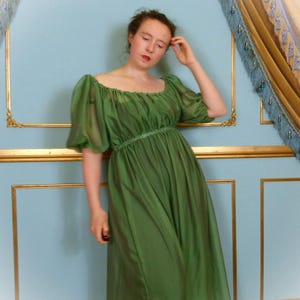 Op de afbeelding: Een lange, vloeiende groene jurk met korte, gepofte mouwen en een gerimpelde taille. De jurk heeft een vierkante halslijn en een zachte, draperende stof. De jurk is effen en felgroen.
