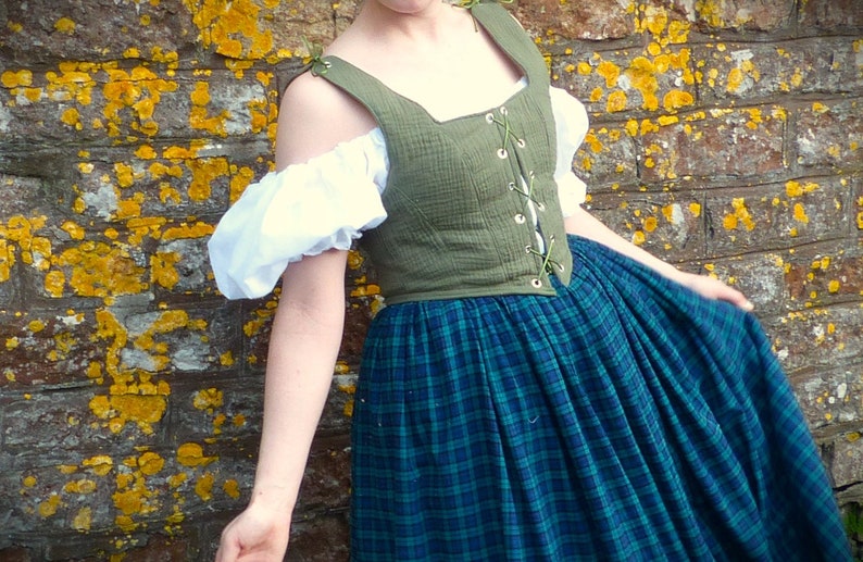 May include: A woman wearing a green linen bodice with a lace-up front and a blue and green plaid skirt. The bodice has a square neckline and is sleeveless. The skirt is full and gathered at the waist.
