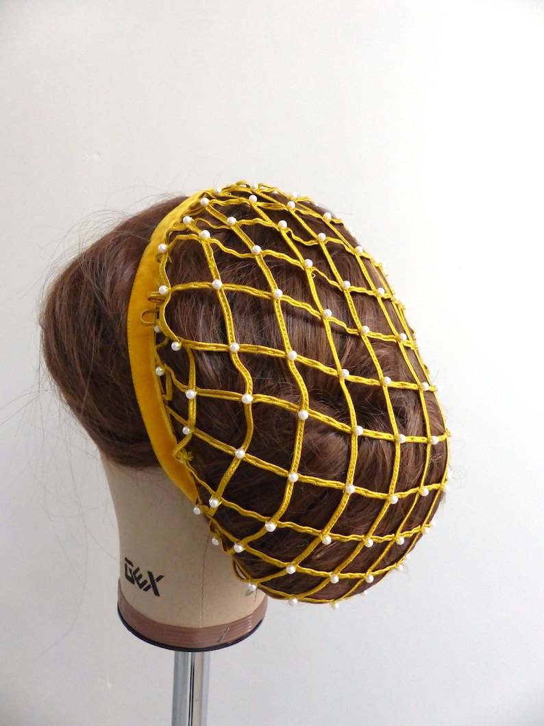 以下が含まれることがあります： ベルベットのバンドと白い真珠のアクセントが付いた黄色のヘアネット。ネットは髪を所定の位置に保持するように設計されています。