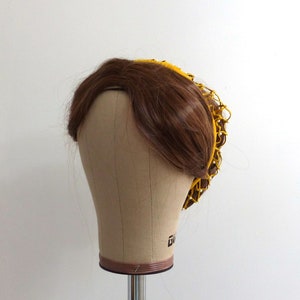 以下が含まれることがあります： 茶色のウィッグに黄色のメッシュのヘアネットが付いている。ヘアネットは円形で、織られた素材で作られている。