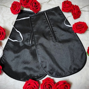 May include: A pair of black satin fabric garment pieces with a white trim and a zipper detail. The pieces are laid out on a white surface with red roses scattered around them.