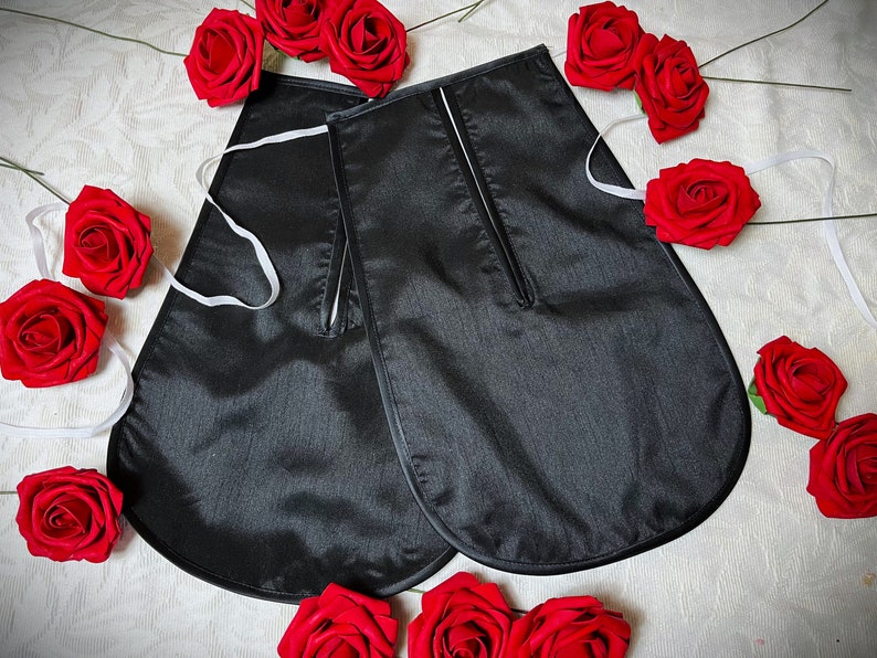 May include: A pair of black satin fabric garment pieces with a white trim and a zipper detail. The pieces are laid out on a white surface with red roses scattered around them.