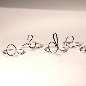 May include: Five silver rings with different designs. The rings are made of thin wire and are delicate in appearance.