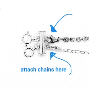 Può includere: Chiusura a T in argento con due anelli di giunzione e due catene attaccate. Il testo "attach chains here" è scritto sotto la chiusura.