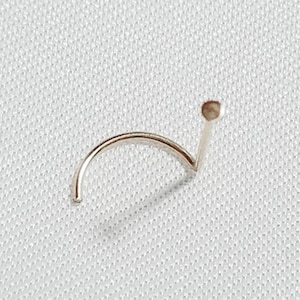 May include: A silver nose ring with a small ball at the end. The ring is curved and has a straight post.