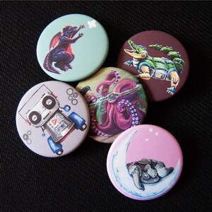 Puede incluir: Conjunto de seis botones redondos de pasador de colores con varias ilustraciones. Los botones presentan un robot, un pulpo, un dragón, un elefante, una luna y un cocodrilo.