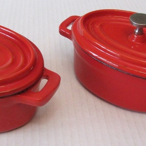 May include: Two red oval cast iron cookware with lids and silver handles.