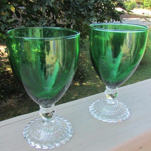 May include: Two green glass goblets with clear glass stems and bases. The bases have a scalloped design.