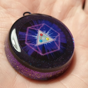 May include: A round, purple resin pendant with a silver-colored geometric design and a small, colorful triangle in the center.