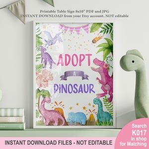 May include: A framed 8x10 inch printable sign with the text "ADOPT A DINOSAUR". The sign features watercolor illustrations of various dinosaurs in shades of pink, purple, and blue, surrounded by green foliage and a banner. The sign is a digital download.